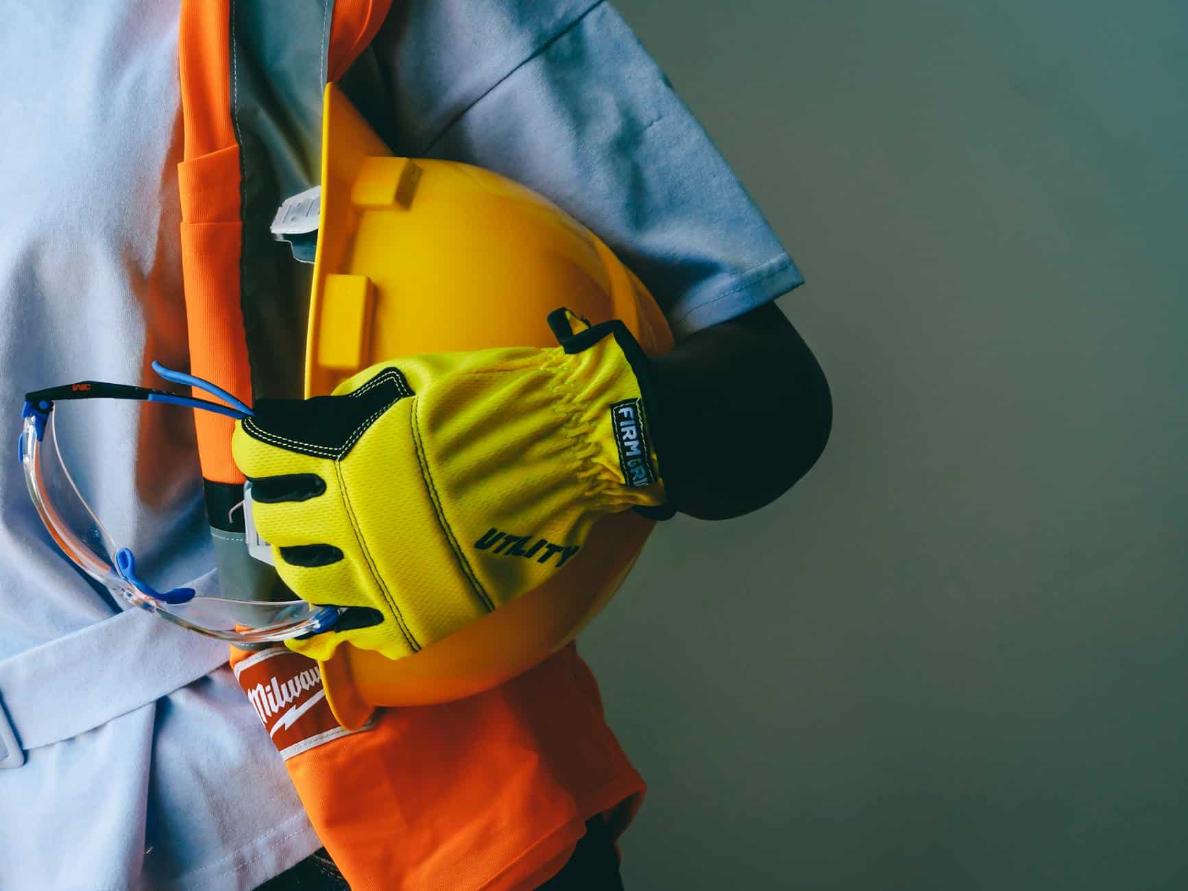 Worker holding a yellow hard hat, safety glasses, and high-visibility gloves — personal protective equipment close-up